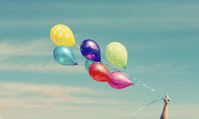 Troubles and feelings of sadness are attached to big, colorful helium balloons and are floating off into a clear blue sky.